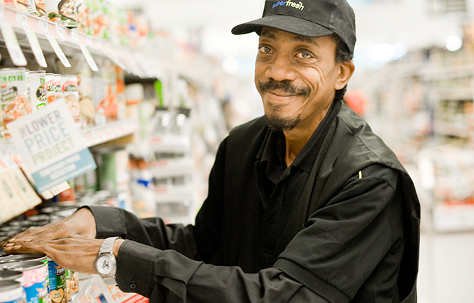 Smiling man in a black hat and jacket standing in supermarket aisle